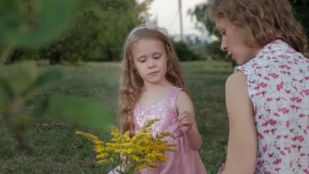 Una madre e una figlia felici stanno bevendo il tè sul velo. Famiglia in un parco cittadino durante un picnic in una calda serata al tramonto . — Video Stock