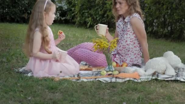 Una madre y una hija felices están bebiendo té en el velo. Familia en un parque de la ciudad en un picnic en una cálida noche al atardecer . — Vídeos de Stock