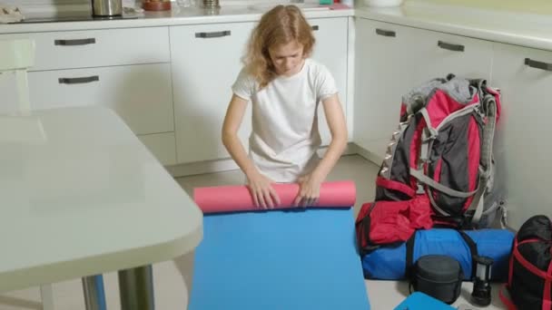 Uma turista recolhe coisas em uma mochila na cozinha da casa e se prepara para uma viagem — Vídeo de Stock