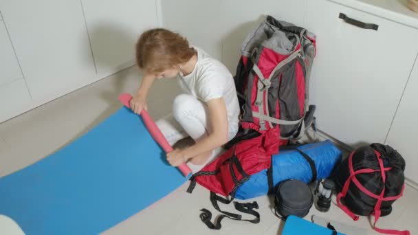 Une touriste femme recueille des choses dans un sac à dos dans la cuisine de la maison et se prépare pour un voyage — Video