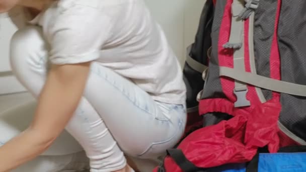 Uma turista recolhe coisas em uma mochila na cozinha da casa e se prepara para uma viagem — Vídeo de Stock