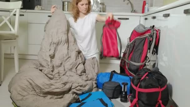 Uma turista recolhe coisas em uma mochila na cozinha da casa e se prepara para uma viagem — Vídeo de Stock