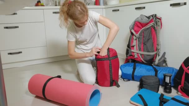 Uma turista recolhe coisas em uma mochila na cozinha da casa e se prepara para uma viagem — Vídeo de Stock