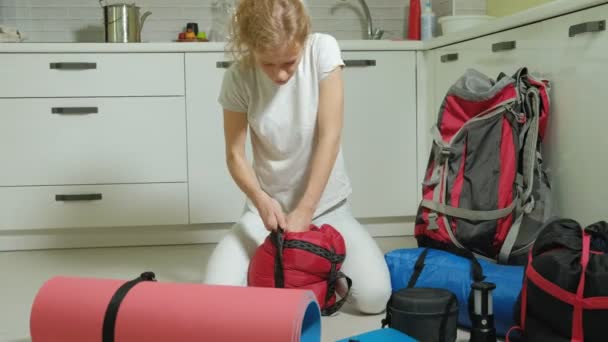 Жінка-турист збирає речі в рюкзаку на кухні будинку і готується до поїздки — стокове відео
