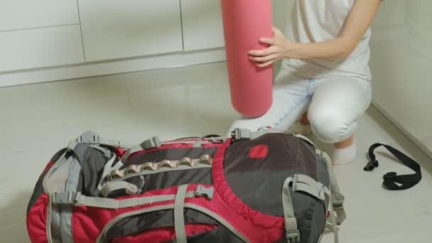 A woman tourist collects things in a backpack in the kitchen of the house and prepares for a trip