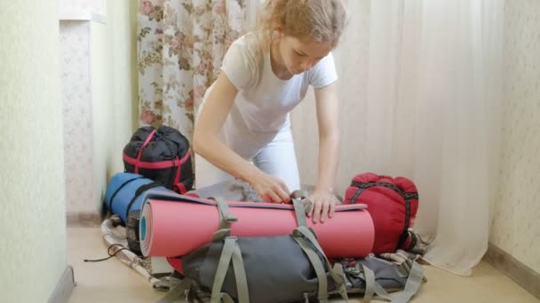 Seorang wanita turis mengumpulkan barang-barang di dalam ransel di dapur rumah dan bersiap-siap untuk melakukan perjalanan — Stok Video