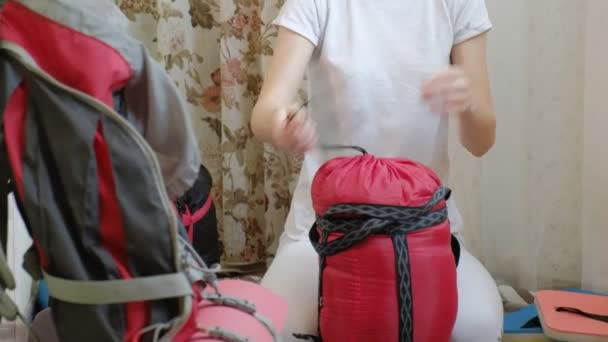 En kvinna turist samlar in saker i en ryggsäck i köket i huset och förbereder för en resa — Stockvideo