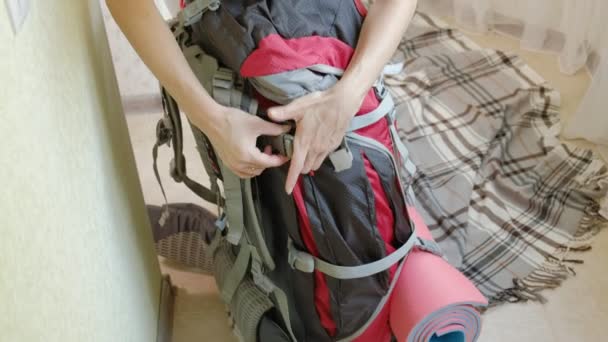 Женщина-туристка собирает вещи в рюкзаке на кухне дома и готовится к поездке — стоковое видео