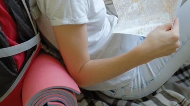 Жінка-турист збирає речі в рюкзаку на кухні будинку і готується до подорожі дивиться на карту паперу — стокове відео