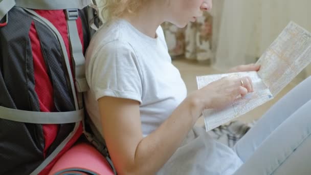 Turista mulher recolhe coisas em uma mochila na cozinha da casa e se prepara para a viagem olha para o mapa de papel — Vídeo de Stock