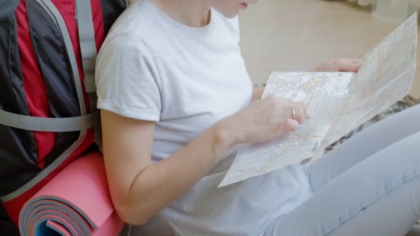 Жінка-турист збирає речі в рюкзаку на кухні будинку і готується до подорожі дивиться на карту паперу — стокове відео