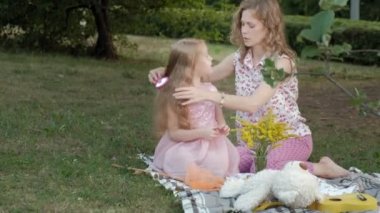 Mutlu bir anne kız saçları tarak. Sıcak bir akşam günbatımında pikniğe üzerinde bir şehir parkı ailesinde. 4k