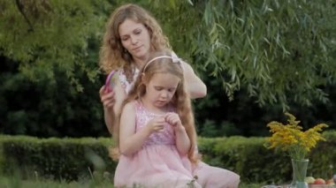 Mutlu bir anne kız saçları tarak. Aile içinde sıcak bir akşam günbatımında pikniğe üzerinde bir şehir parkı.