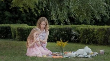 Mutlu bir anne kız saçları tarak. Aile içinde sıcak bir akşam günbatımında pikniğe üzerinde bir şehir parkı.