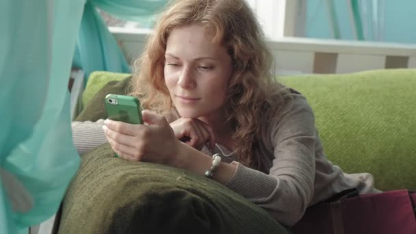 Жінка використовує додаток на смартфоні в кафе, посміхаючись і смс на мобільному телефоні. Красива мультикультурна молода випадкова жінка-професіонал на мобільному телефоні — стокове відео