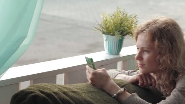Mujer usando la aplicación en el teléfono inteligente en la cafetería sonriendo y mensajes de texto en el teléfono móvil. Hermosa joven multicultural casual profesional femenino en el teléfono móvil — Vídeos de Stock