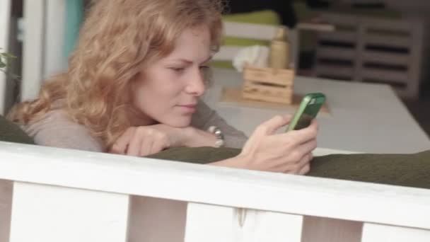 Mulher usando aplicativo no smartphone no café sorrindo e mensagens de texto no telefone celular. Bela multicultural jovem casual profissional feminino no telefone móvel — Vídeo de Stock