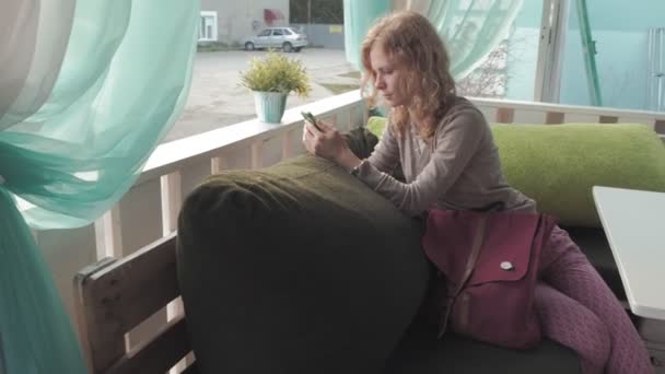 Mujer usando la aplicación en el teléfono inteligente en la cafetería sonriendo y mensajes de texto en el teléfono móvil. Hermosa joven multicultural casual profesional femenino en el teléfono móvil — Vídeo de stock