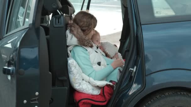 Hermosa joven y su hija pequeña están sentados en el maletero abierto de un coche en la orilla del río del mar disfrutando de un ordenador portátil — Vídeos de Stock