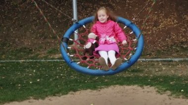 Oyun alanında yuvarlak bir salıncak üzerinde pembe elbise giymiş küçük bir kız salıncaklar