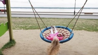 Oyun alanında yuvarlak bir salıncak üzerinde pembe elbise giymiş küçük bir kız salıncaklar