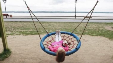 Oyun alanında yuvarlak bir salıncak üzerinde pembe elbise giymiş küçük bir kız salıncaklar