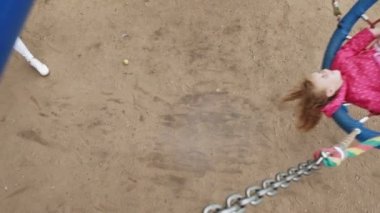 Oyun alanında yuvarlak bir salıncak üzerinde pembe elbise giymiş küçük bir kız salıncaklar