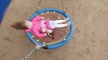 Oyun alanında yuvarlak bir salıncak üzerinde pembe elbise giymiş küçük bir kız salıncaklar