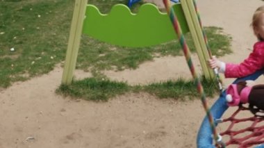 Oyun alanında yuvarlak bir salıncak üzerinde pembe elbise giymiş küçük bir kız salıncaklar