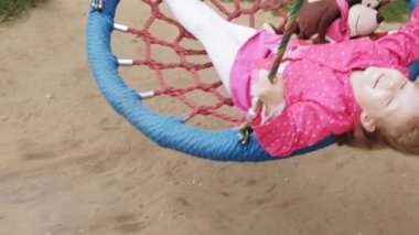 Oyun alanında yuvarlak bir salıncak üzerinde pembe elbise giymiş küçük bir kız salıncaklar
