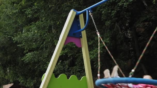 Uma menina em um vestido rosa balança em um balanço redondo no playground — Vídeo de Stock