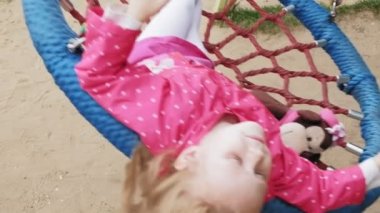Oyun alanında yuvarlak bir salıncak üzerinde pembe elbise giymiş küçük bir kız salıncaklar