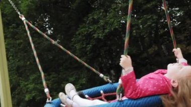 Oyun alanında yuvarlak bir salıncak üzerinde pembe elbise giymiş küçük bir kız salıncaklar