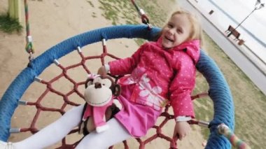 Oyun alanında yuvarlak bir salıncak üzerinde pembe elbise giymiş küçük bir kız salıncaklar