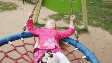 Oyun alanında yuvarlak bir salıncak üzerinde pembe elbise giymiş küçük bir kız salıncaklar