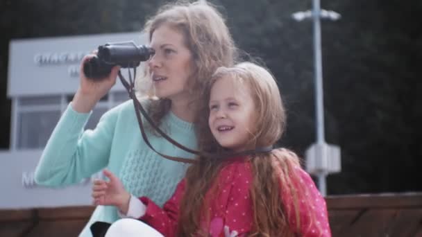 Женщина с дочерью смотрит в бинокль на пляже — стоковое видео