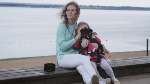 Жінка з дочкою дивиться через бінокль на пляжі — стокове відео