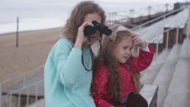 Eine Frau mit ihrer Tochter blickt durch ein Fernglas auf den Strand — Stockvideo