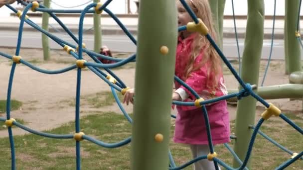 Uma menina em um vestido rosa e sua mãe estão brincando com uma escada de corda no playground — Vídeo de Stock