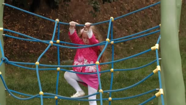 Ein kleines Mädchen im rosa Kleid und ihre Mutter spielen mit einer Strickleiter auf dem Spielplatz — Stockvideo