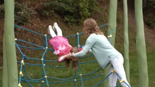 Ein kleines Mädchen im rosa Kleid und ihre Mutter spielen mit einer Strickleiter auf dem Spielplatz — Stockvideo