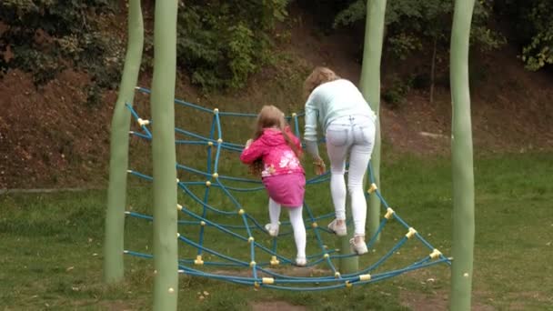 Una niña con un vestido rosa y su madre están jugando con una escalera de cuerda en el patio de recreo — Vídeos de Stock