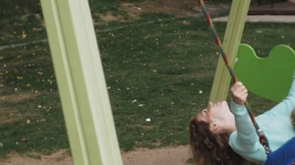 A little girl in a pink dress and her mother swinging on a round swing at the playground — Stock Video