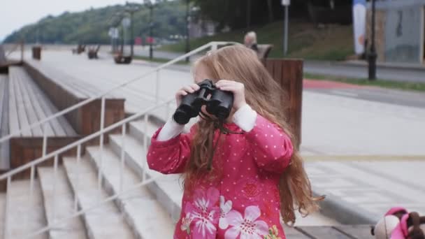Lilla vackra flicka tittar genom kikaren på stranden — Stockvideo