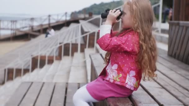 Маленька красива дівчинка дивиться через бінокль на пляжі — стокове відео