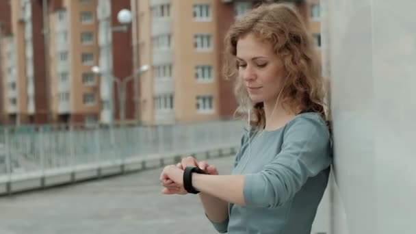 Hübsche lächelnde Fitness-Frau mit Lauf-App vor dem Lauf, um das Tempo auf der Smartwatch zu verfolgen, glücklich lächelndes sportliches Mädchen per SMS vor dem morgendlichen Training — Stockvideo