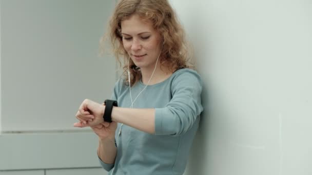 Mujer fitness bastante sonriente utilizando la aplicación de ejecución antes de la carrera para rastrear el ritmo en smartwatch, feliz chica deportiva sonriente mensaje de texto en el teléfono inteligente antes del entrenamiento de la mañana — Vídeos de Stock