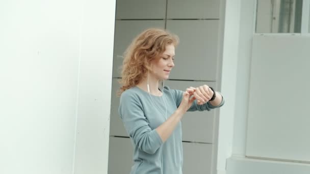 Ganska leende fitness kvinna appen körs innan körningen för spår takten på smartwatch, glada leende sportig tjej SMS meddelande på smartphone innan morgon träningspass — Stockvideo