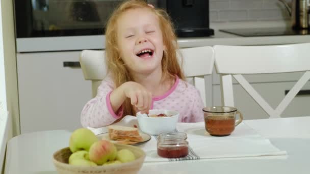 Little girl eating porridge in the kitchen at home — Stock Video