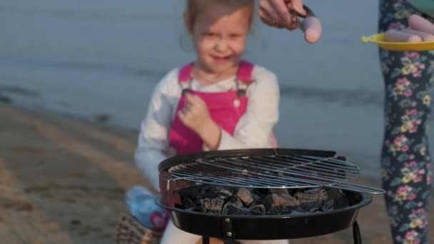 Moeder en dochter bak vlees en groenten op een barbecue op het strand op het strand — Stockvideo